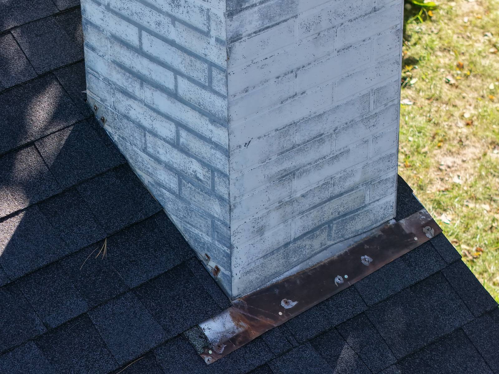 Close-up of a white brick chimney showing rusted step and counter flashing on dark asphalt shingles